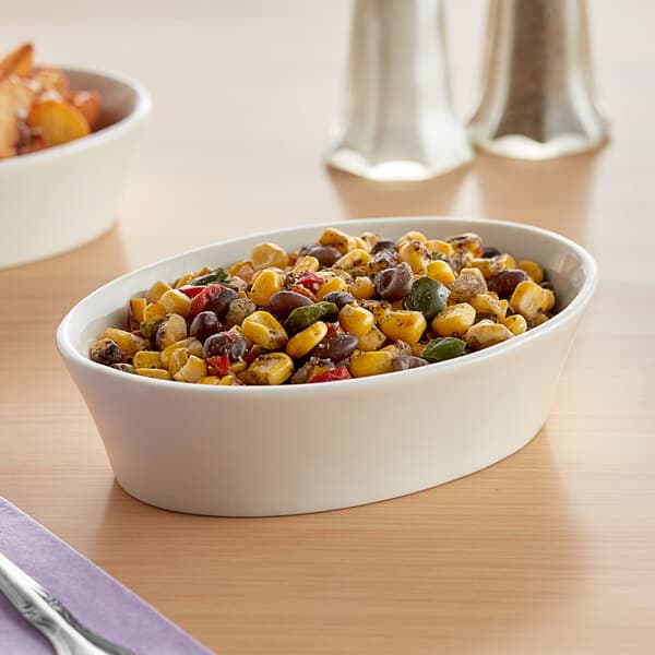 An Acopa ivory oval stoneware bowl filled with corn and beans on a table.