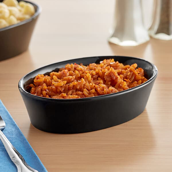 A bowl of rice in an Acopa black stoneware baker dish on a table with silverware.