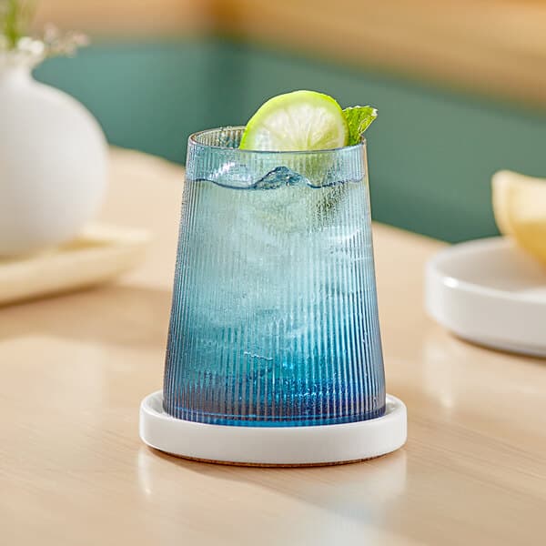 An Acopa Lore blue stemless wine glass with a drink, ice, and a lime slice on a table.