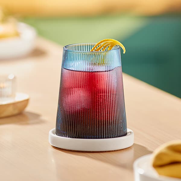 An Acopa Lore blue stemless wine glass with a drink and a lemon peel on a table.