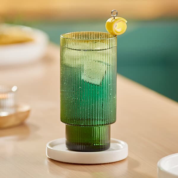 A green Acopa Lore highball glass with a drink and lemon wedge.