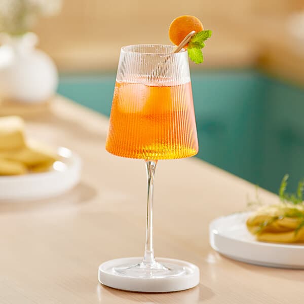 An Acopa Lore wine glass filled with orange juice and a straw on a table.