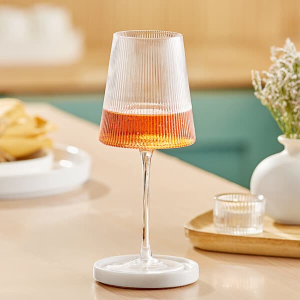 An Acopa Lore wine glass filled with wine on a table with flowers.