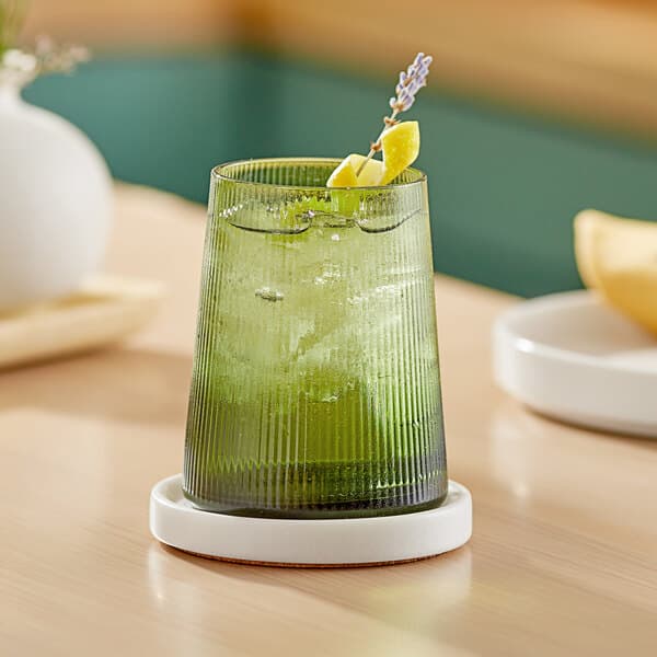 A green stemless wine glass with a drink and lemon on a table.