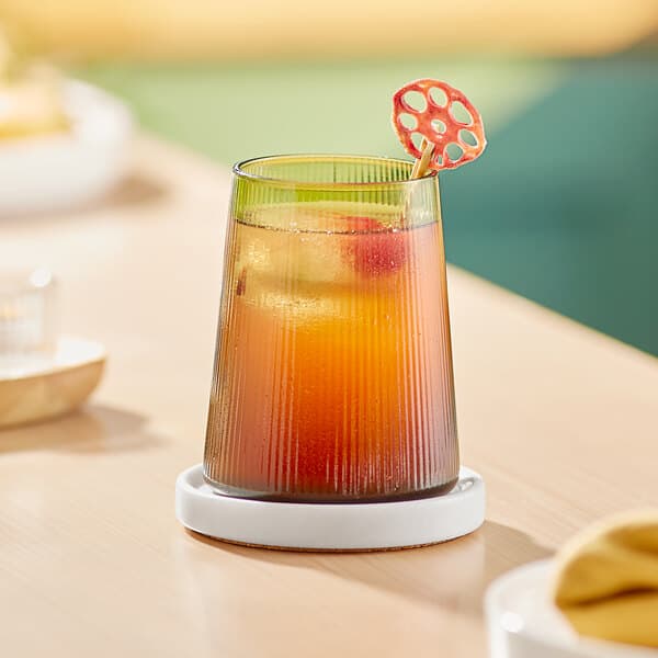 A green stemless wine glass filled with a yellow drink and a red garnish.