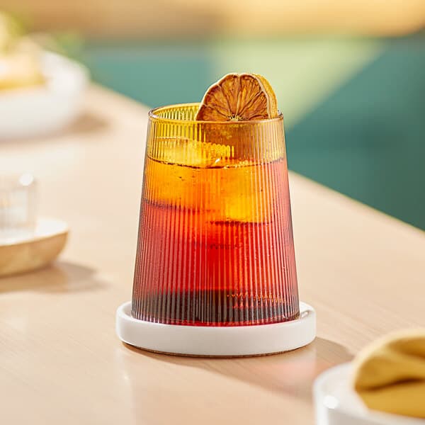 An Acopa Lore amber stemless wine glass filled with orange liquid and a slice of orange on top.