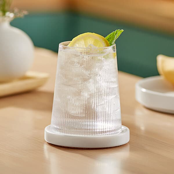 An Acopa Lore stemless wine glass with ice and a lemon slice on a table.
