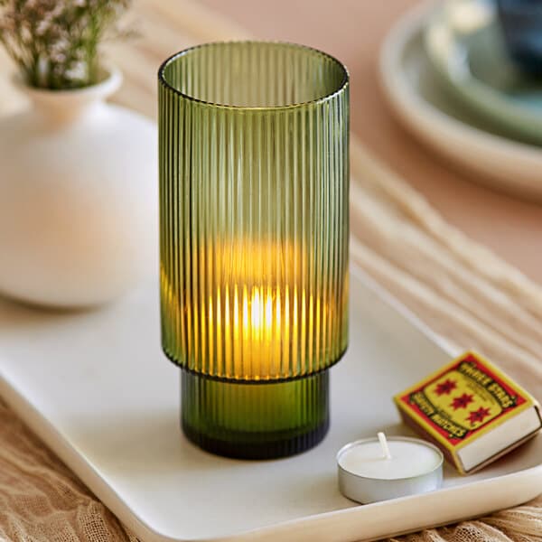 A green glass Acopa Lore tealight holder with a lit candle inside.