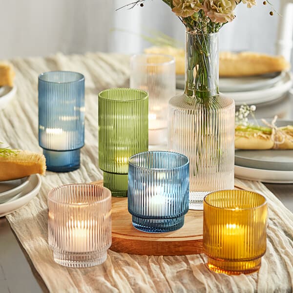 A group of Acopa green glass tealight holders with candles on a table with flowers.