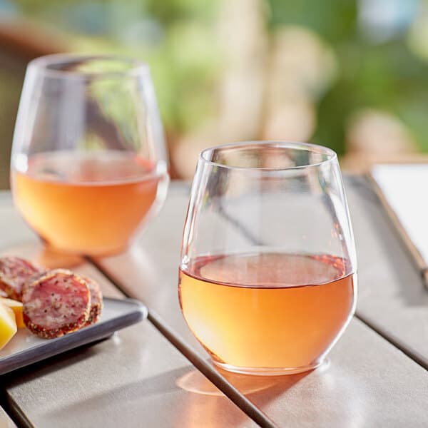 Two Acopa Endure plastic stemless wine glasses on a table outdoors with food.