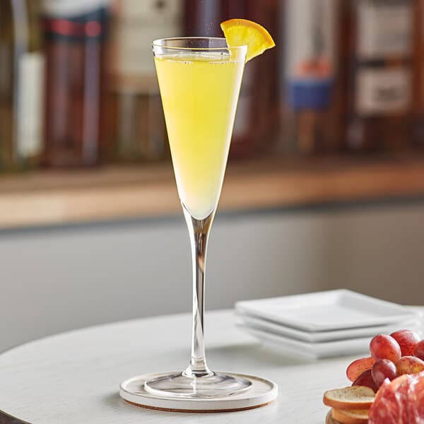 A close-up of a Trumpet Flute glass filled with yellow liquid and a slice of orange.