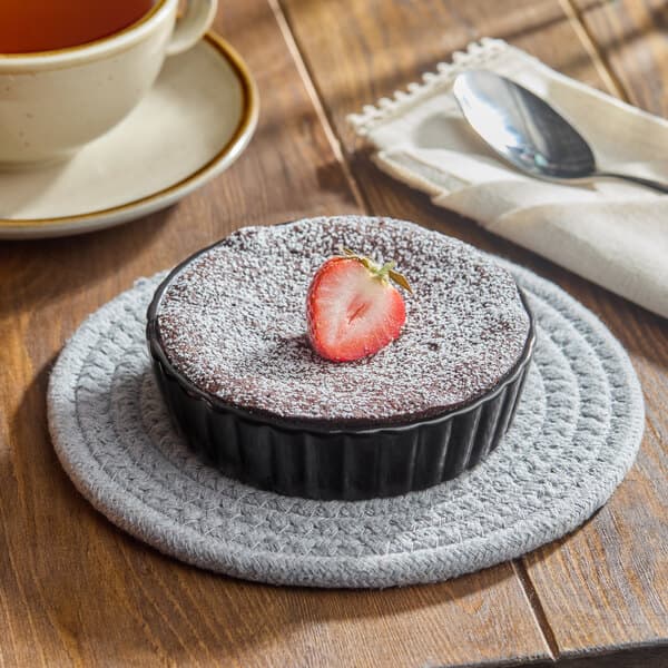 A chocolate dessert in an Acopa Keystone porcelain souffle dish with a strawberry on top on a table with a cup of tea.