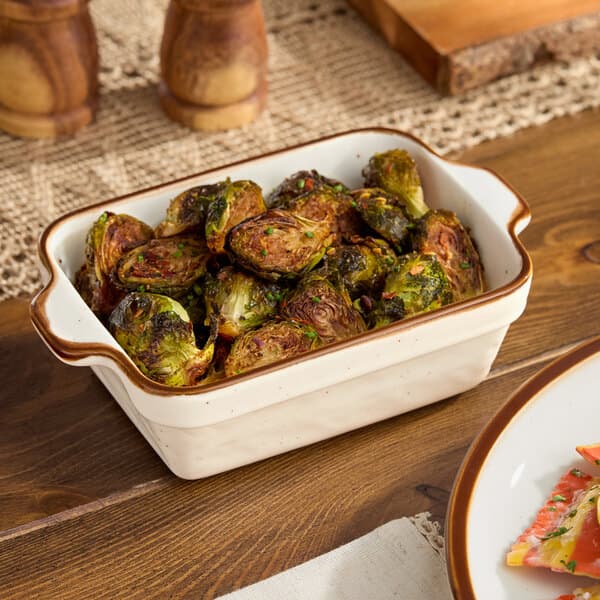 A white Acopa Keystone rectangular casserole dish filled with roasted brussels sprouts on a table.