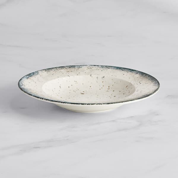 An Acopa Architect white porcelain bowl with blue specks on a marble surface.