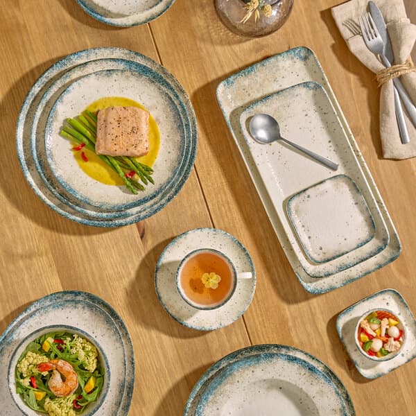 A set of gray porcelain wide rim bowls and plates arranged on a wooden table with food and utensils.