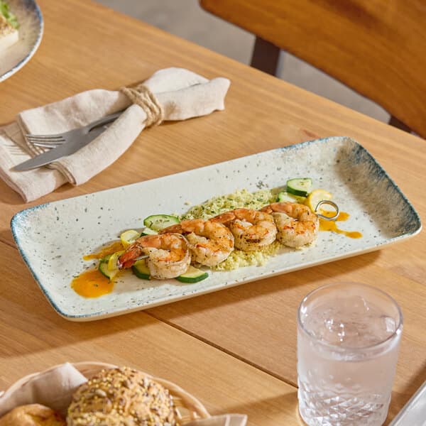A rectangular gray porcelain platter displaying a shrimp and vegetable dish on a wooden table.