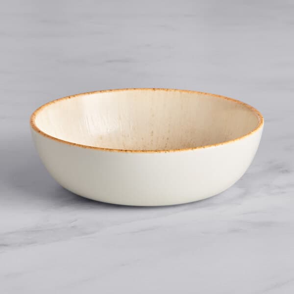 An Acopa Cape beige porcelain bowl with a brown rim on a marble surface.