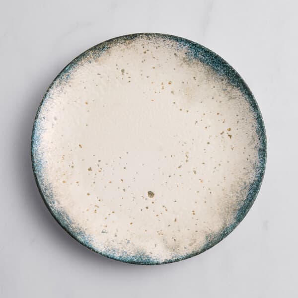 An Acopa Architect gray porcelain coupe plate with white and blue speckles on it.