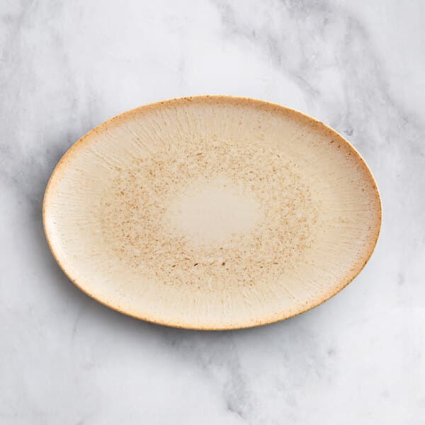 An Acopa beige porcelain oval platter on a marble surface.