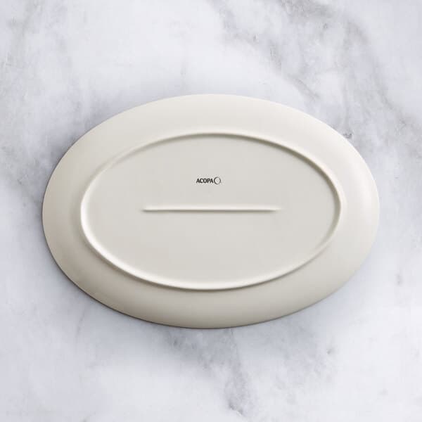 An Acopa Cape beige oval porcelain platter on a marble surface.