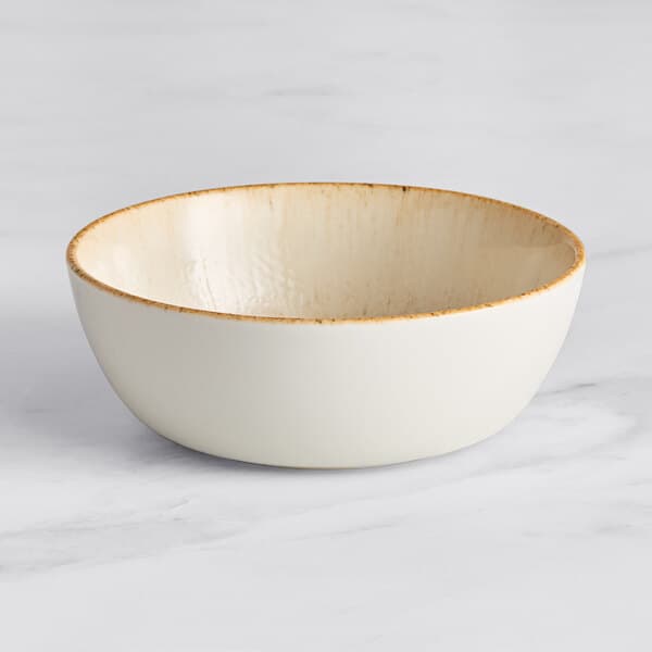 A beige porcelain bowl with a brown rim on a marble surface.