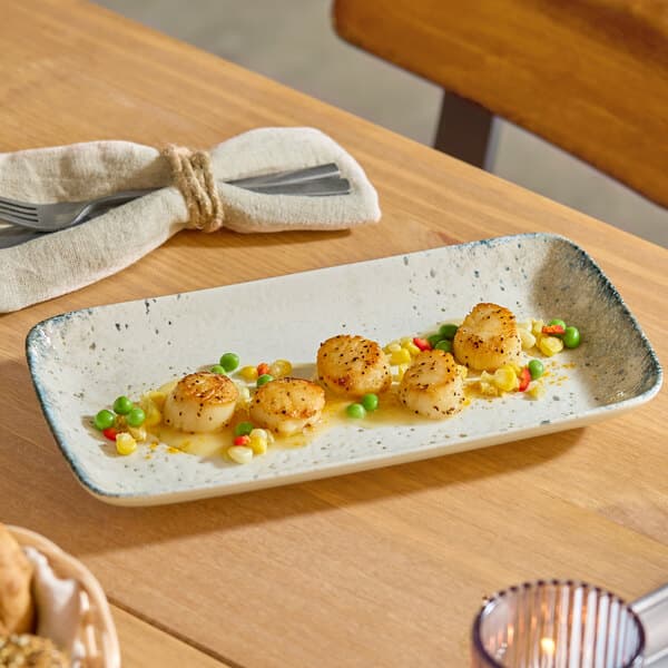 A rectangular gray porcelain platter displaying seared scallops with mixed vegetables.