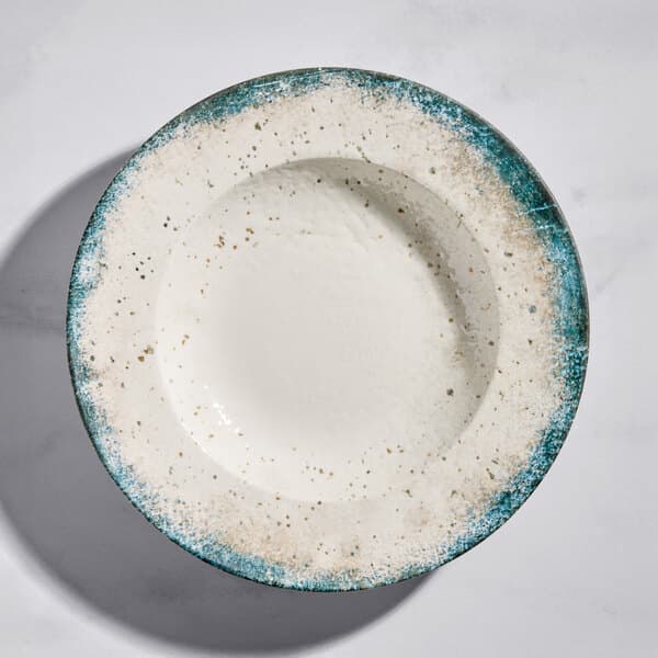 A round gray porcelain wide rim bowl with a speckled design and blue-green edge.