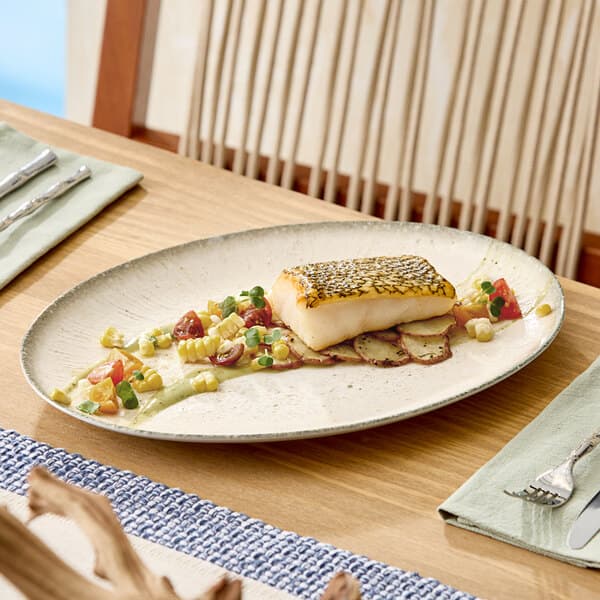 An oval gray porcelain platter displaying a plated fish dish with vegetables on a wooden table.