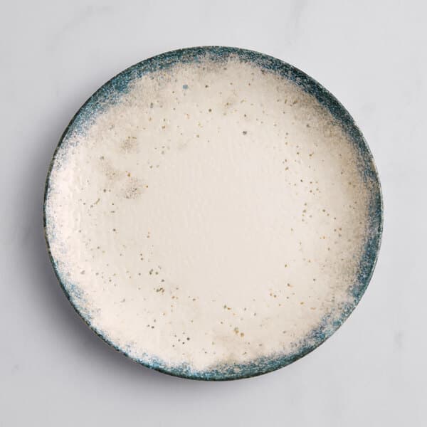 An Acopa Architect white porcelain coupe plate with blue speckles.