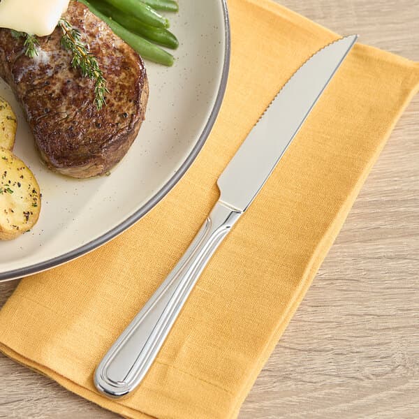 An Acopa Edgeworth steak knife cutting a piece of steak with green beans on a plate.
