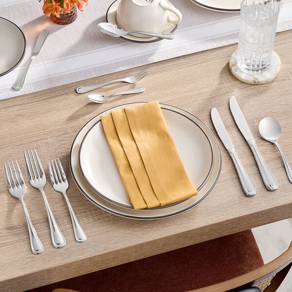 A table with a white plate, napkins, and Acopa Edgeworth stainless steel forks.