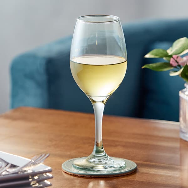 A clear 10.5 oz. all-purpose wine glass partially filled with white wine, placed on a wooden table.