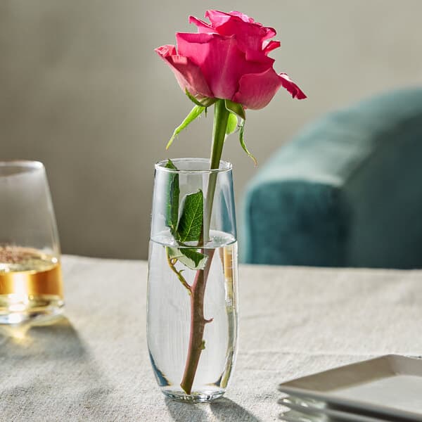 A clear glass bud vase holding a single pink rose with water inside.