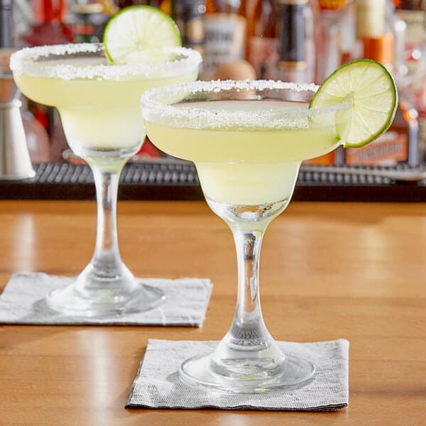 A 9 oz. margarita glass filled with a yellow cocktail, garnished with a lime slice and a salted rim.
