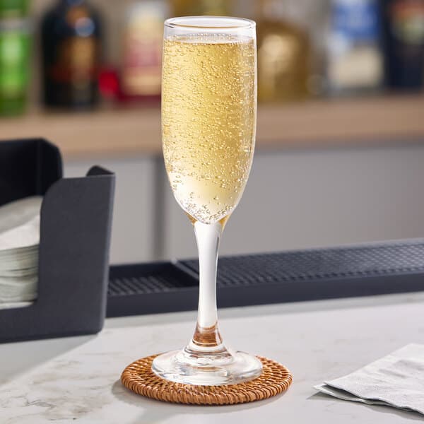 A clear 6 oz. flute glass filled with sparkling beverage, placed on a coaster on a bar counter.